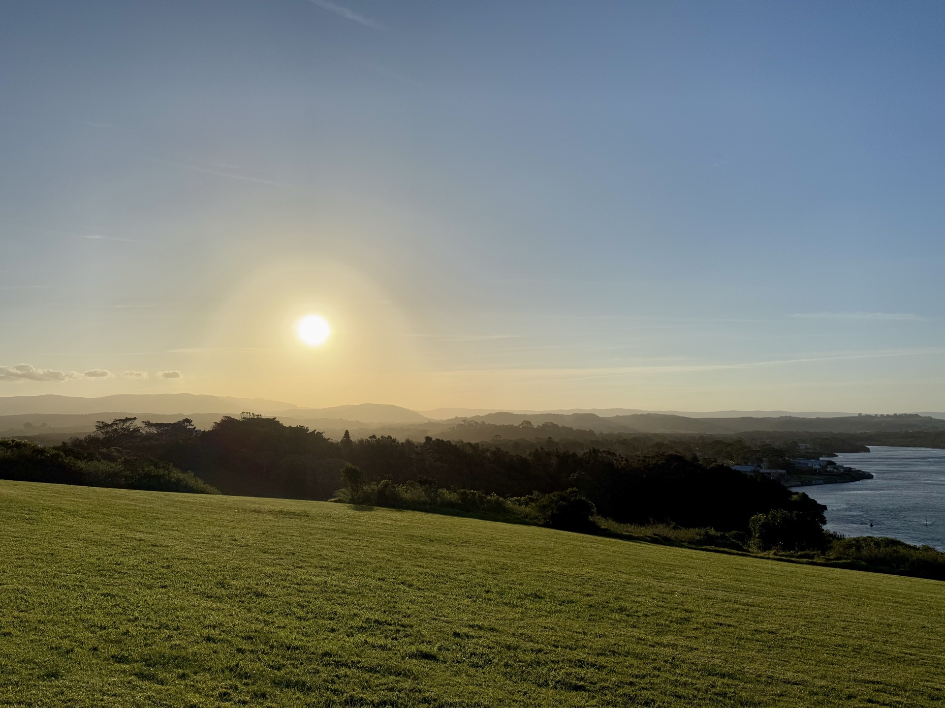 A sunset over rolling green fields meeting the ocean horizon, evoking clear vision and quiet endurance